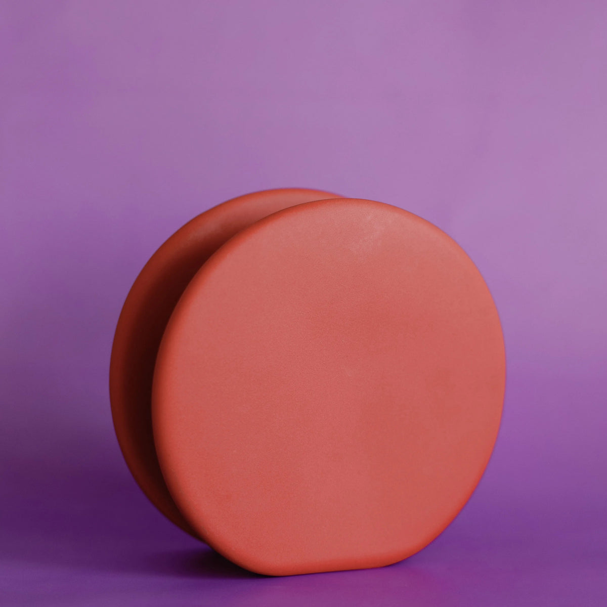 Two terracotta-orange ceramic circle bud vases nested together on a vivid purple backdrop