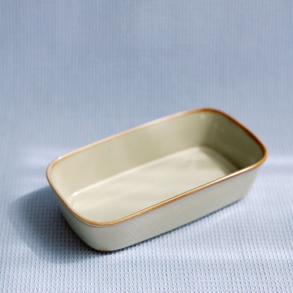 Ceramic glazed rectangular serving dish in cream with a golden-brown rim, on pale blue waffle cloth.