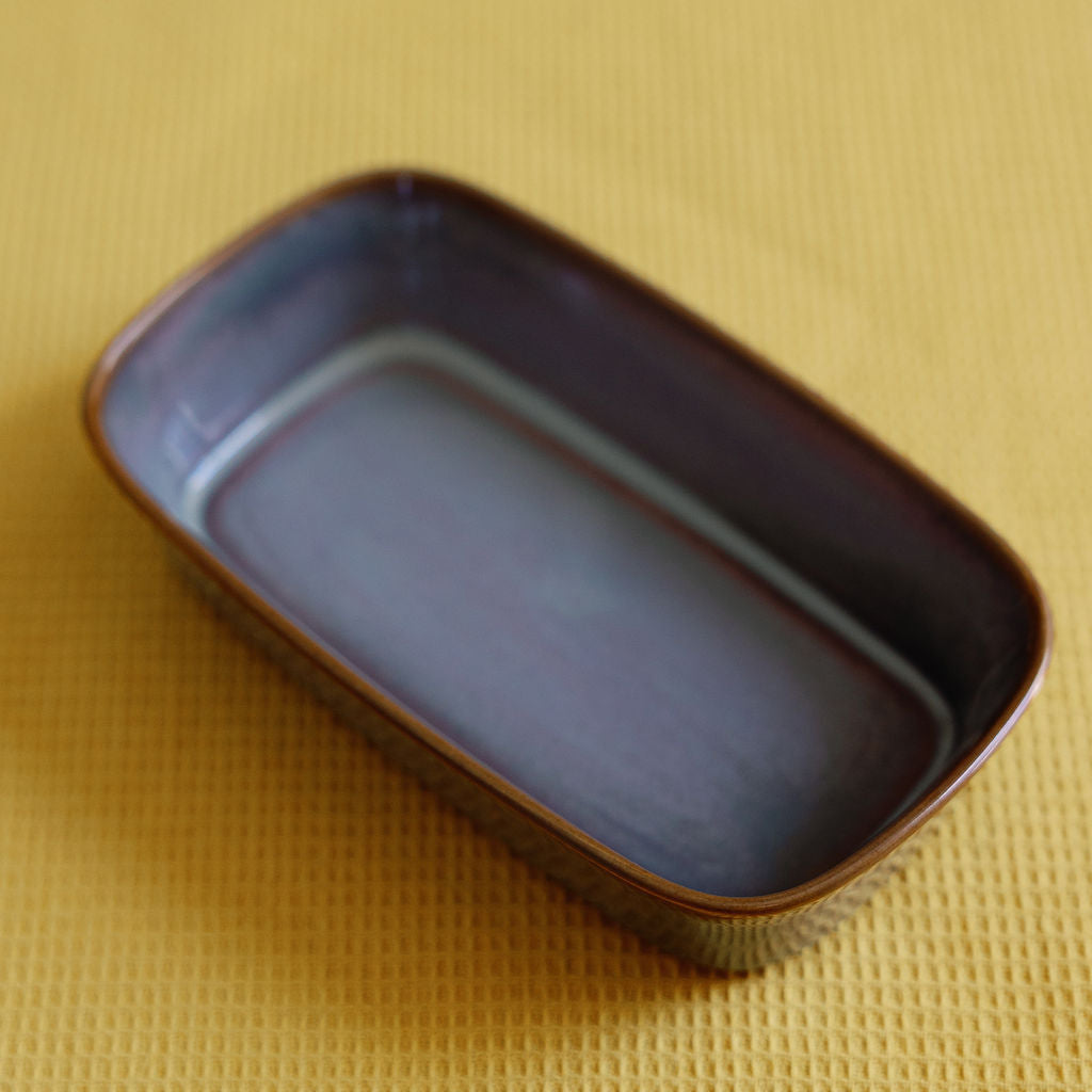 Ceramic glazed serving dish in mottled purple-grey with a brown rim, shown on a yellow textured cloth.