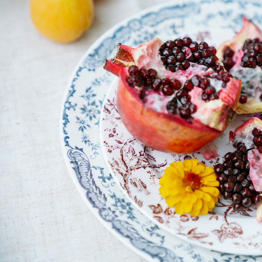 Chantilly Lace porcelain plates styled with cut pomegranate and apricots on a linen table, blue and red floral rims.