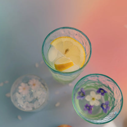 Coastal Hues glasses from above with lemon, ice and floating violets, styled on a pastel ombre surface.