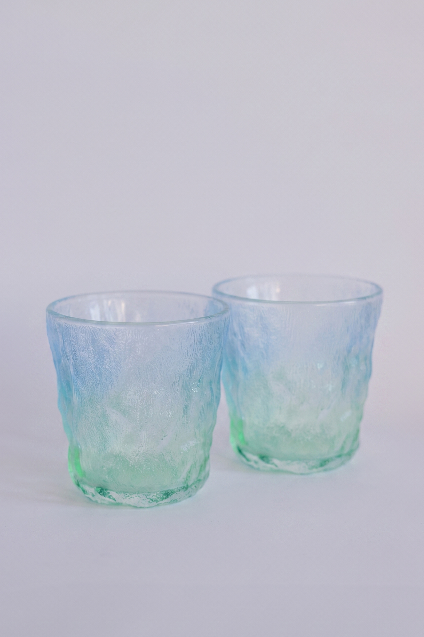 Two textured glass tumblers with a blue and green ombre gradient, photographed on a clean white background.