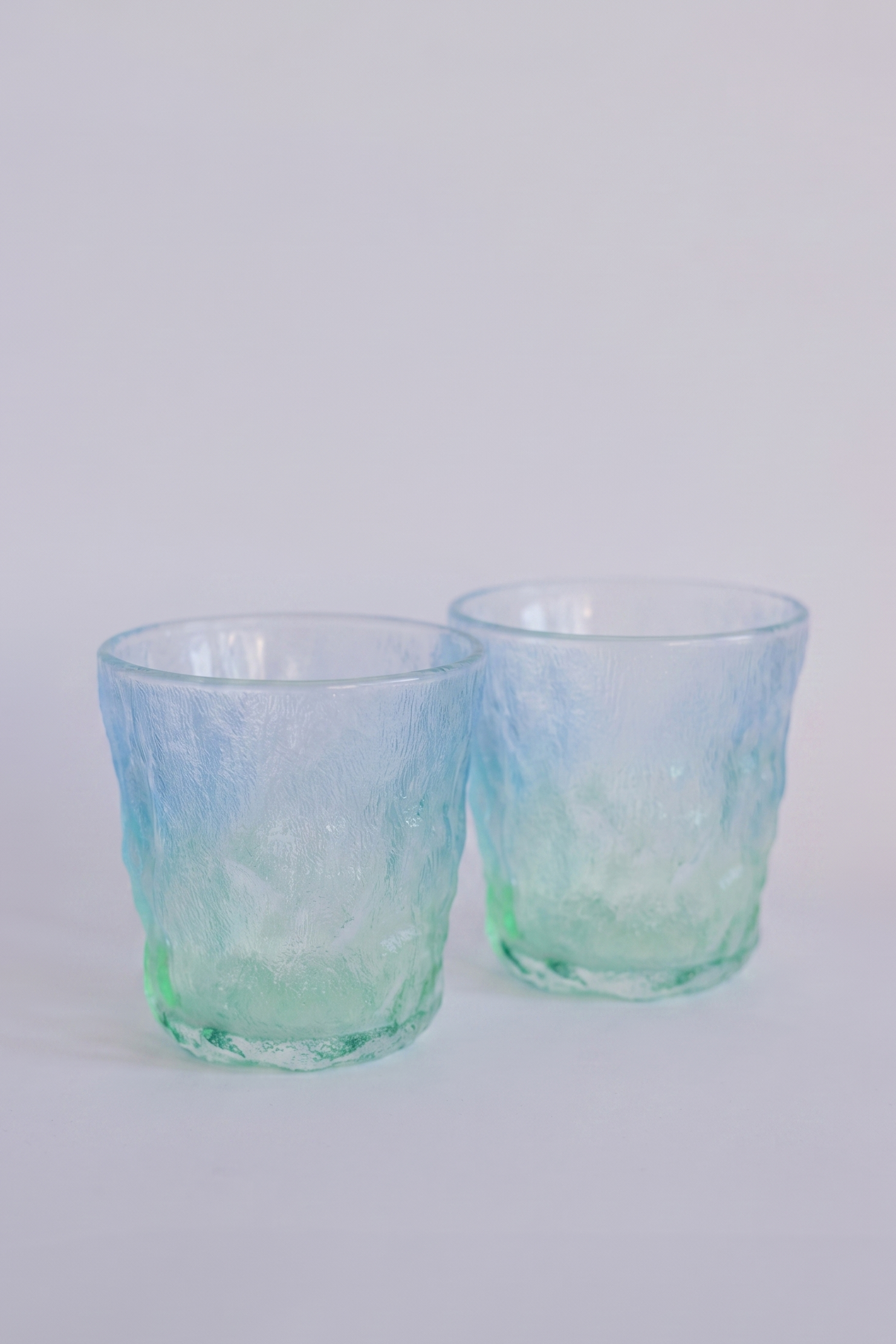 Two textured glass tumblers with a blue and green ombre gradient, photographed on a clean white background.