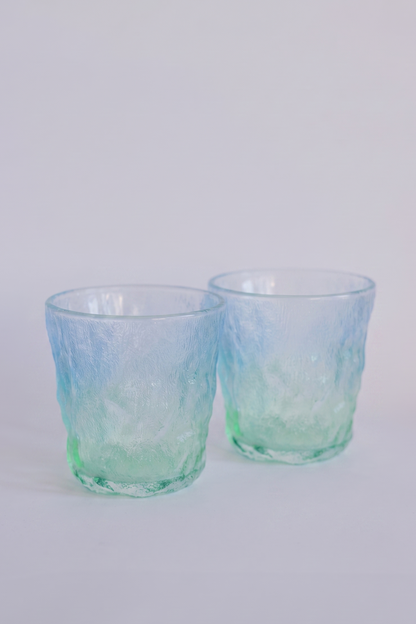Two textured glass tumblers with a blue and green ombre gradient, photographed on a clean white background.
