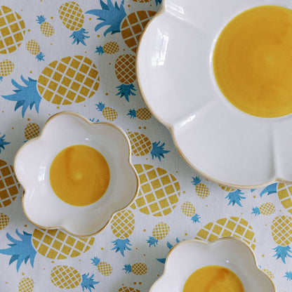 A set table with white flower-shaped plates, yellow centers, surrounded by lemons and floral tablecloth.