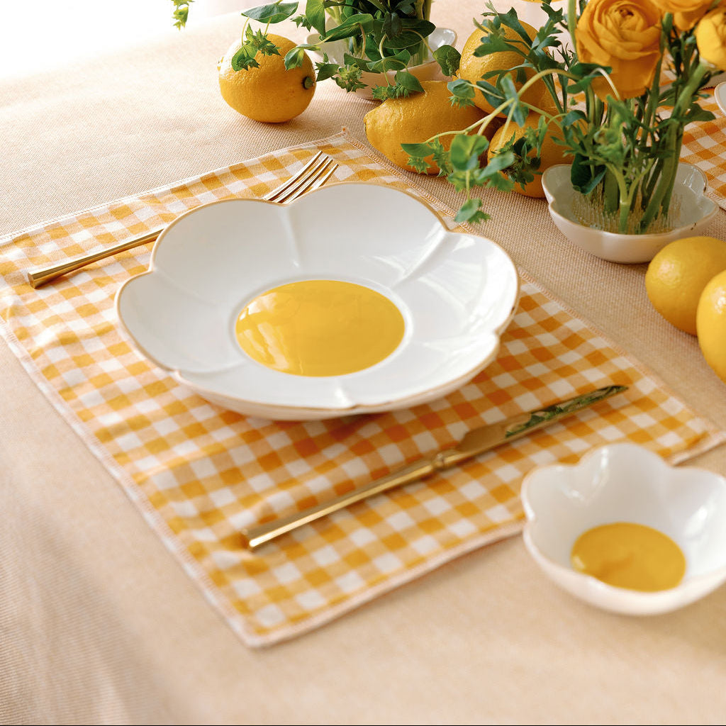 Daisy Bloom porcelain plate with golden yellow center on gingham, set among yellow ranunculus and lemons.