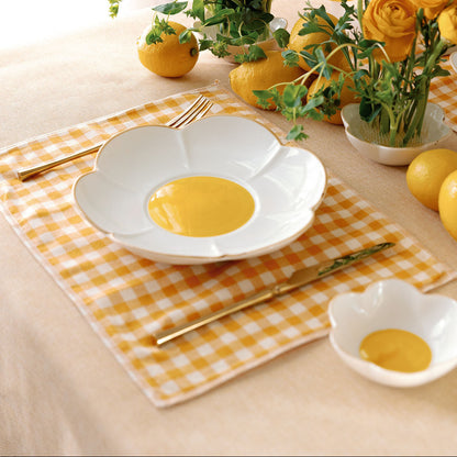 Daisy Bloom porcelain plate with golden yellow center on gingham, set among yellow ranunculus and lemons.
