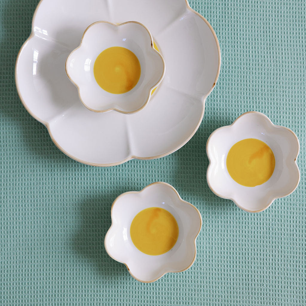Three white ceramic egg-shaped dishes with yellow centers on a light blue textured surface.
