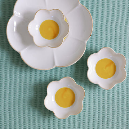 Three white ceramic egg-shaped dishes with yellow centers on a light blue textured surface.