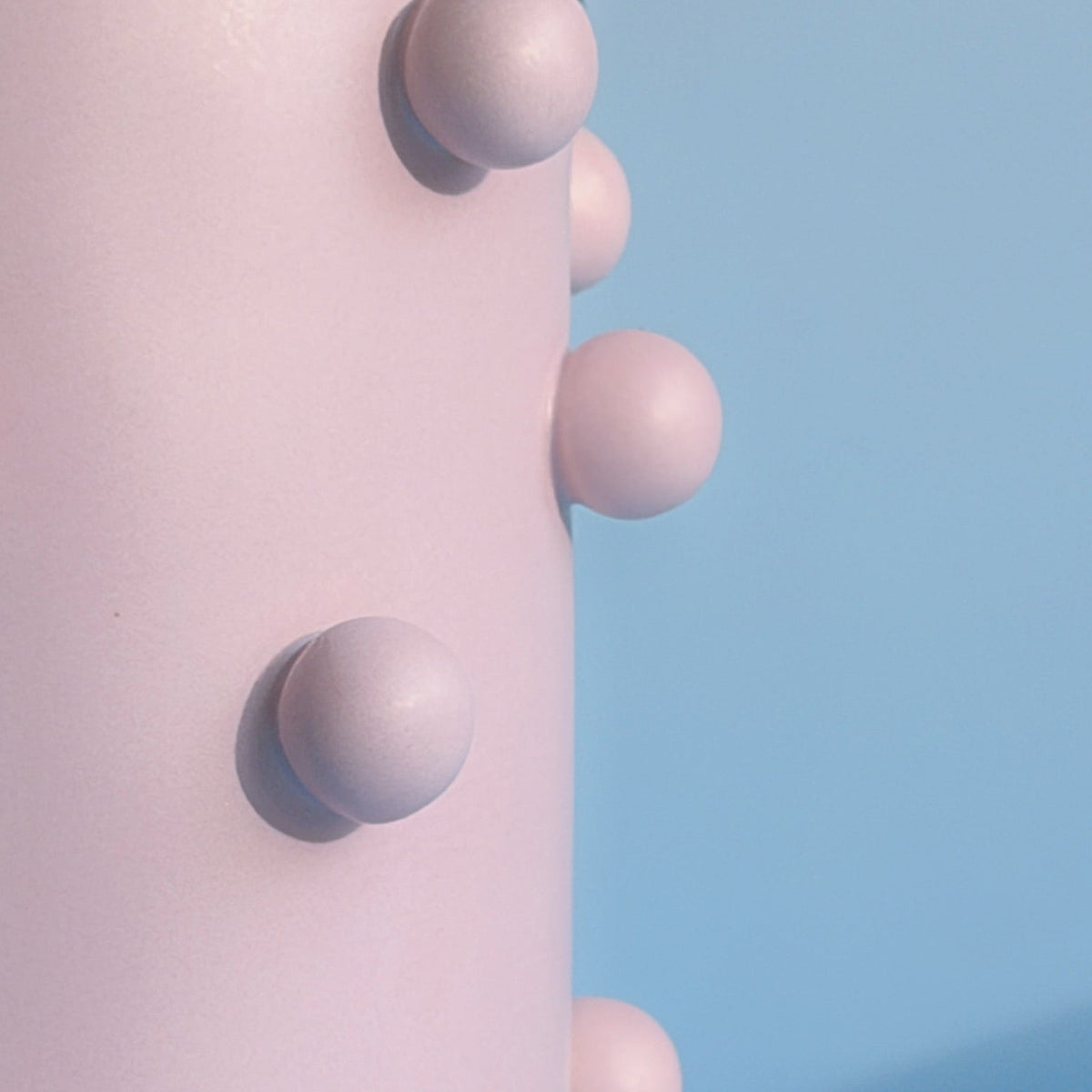 Close-up of raised lavender dot studs on the matte pink Dotty Cylinder Ceramic Vase against blue.