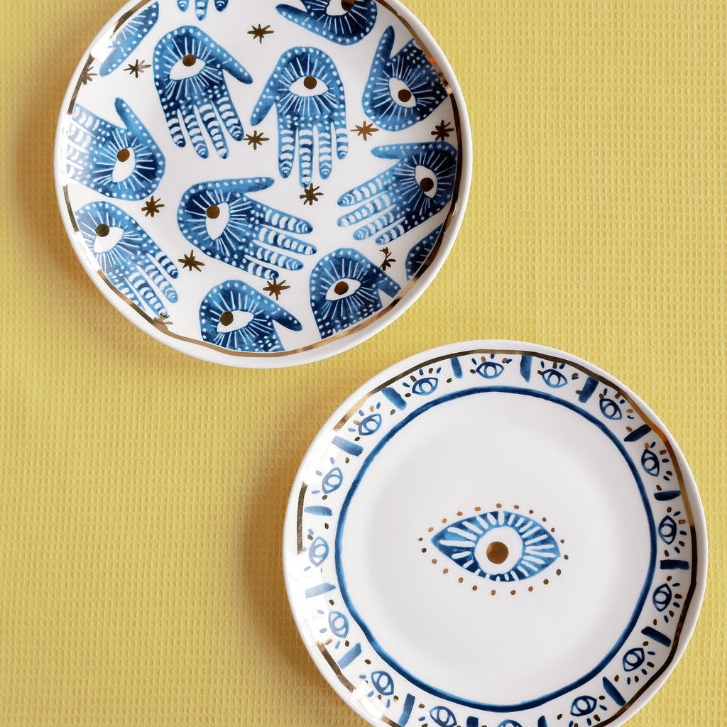 Two Mystic Porcelain Gilded plates with blue hamsa hands and an evil eye motif, gold trim on a yellow surface.