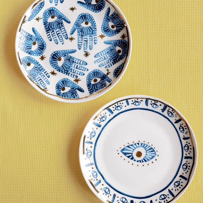 Two Mystic Porcelain Gilded plates with blue hamsa hands and an evil eye motif, gold trim on a yellow surface.