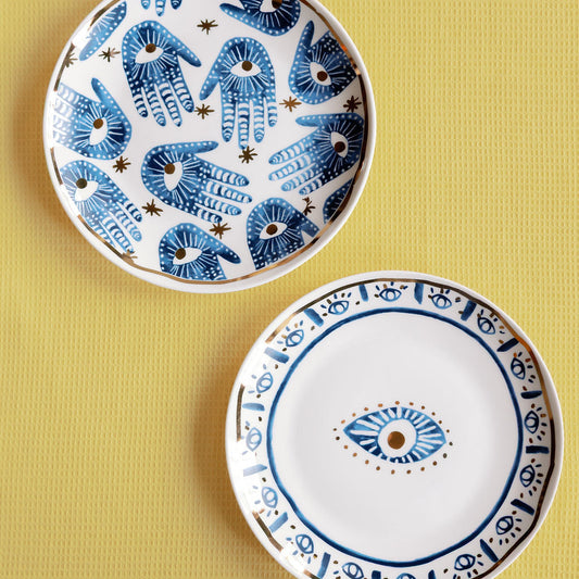 Two Mystic Porcelain Gilded plates with blue hamsa hands and an evil eye motif, gold trim on a yellow surface.