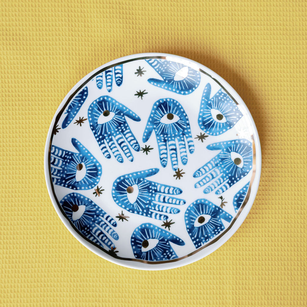 Mystic Porcelain Gilded plate painted with blue hamsa hands, eyes and gold stars on a yellow backdrop.