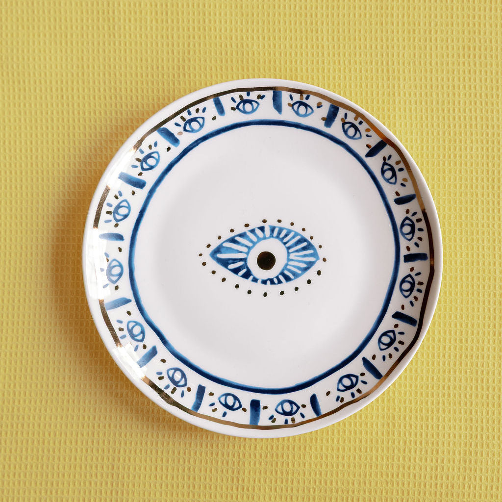 Mystic Porcelain Gilded plate with a central blue evil eye and gold-detailed border, on a yellow surface.