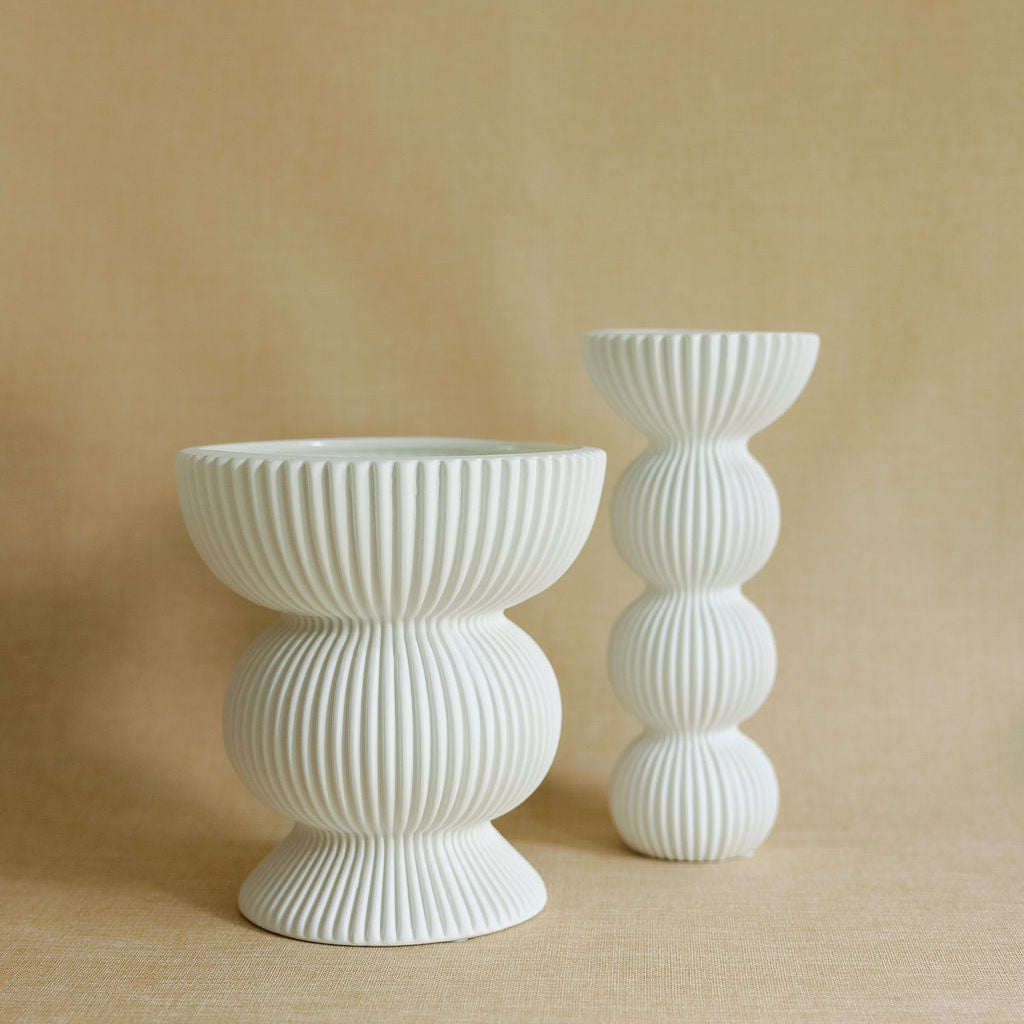 Two white fluted Fluted Column Ceramic Vases, a wide footed bowl and a tall stacked-bubble form, on linen.