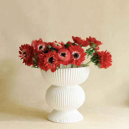 White vase with red flowers on a beige background