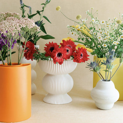 White ribbed Fluted Column Ceramic Vase holding red anemones amid orange and yellow vases of wildflowers.