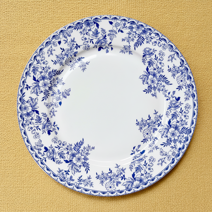 A round white ceramic plate with a blue floral border pattern, photographed from directly above on a textured mustard-yellow surface.