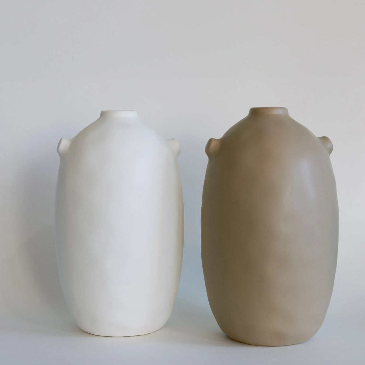Two tall matte Kiln ceramic vases side by side in cream and taupe, with small nub handles at the neck