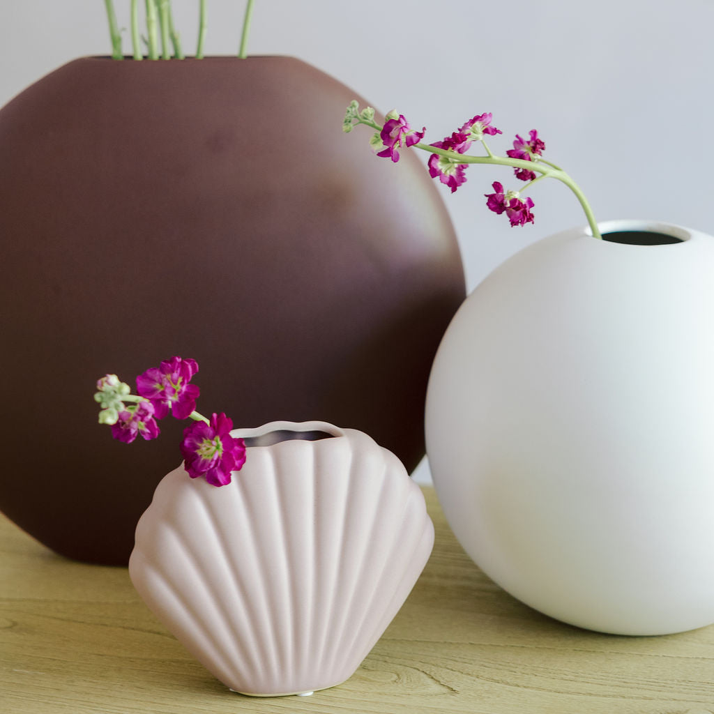 Matte white Large Orb Ceramic Vase styled with a brown vase and pink shell vase holding magenta stock flowers.