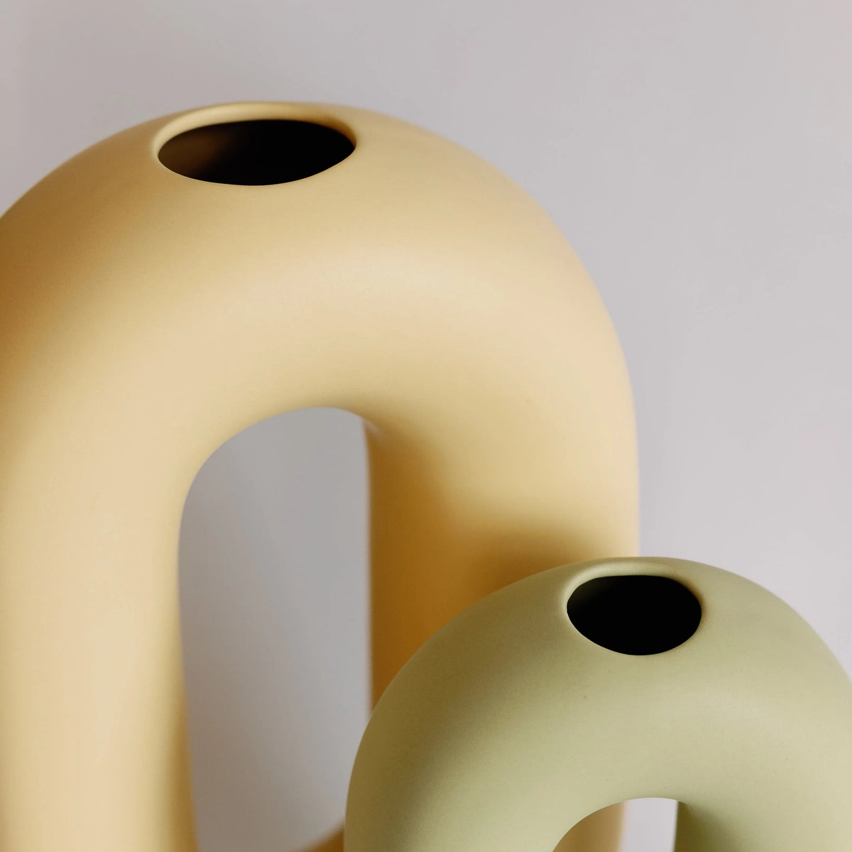 Yellow and sage oval loop bud vases close-up, two sizes overlapping showing the small round top openings