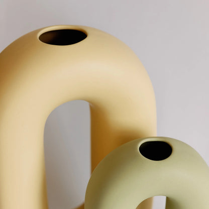 Yellow and sage oval loop bud vases close-up, two sizes overlapping showing the small round top openings