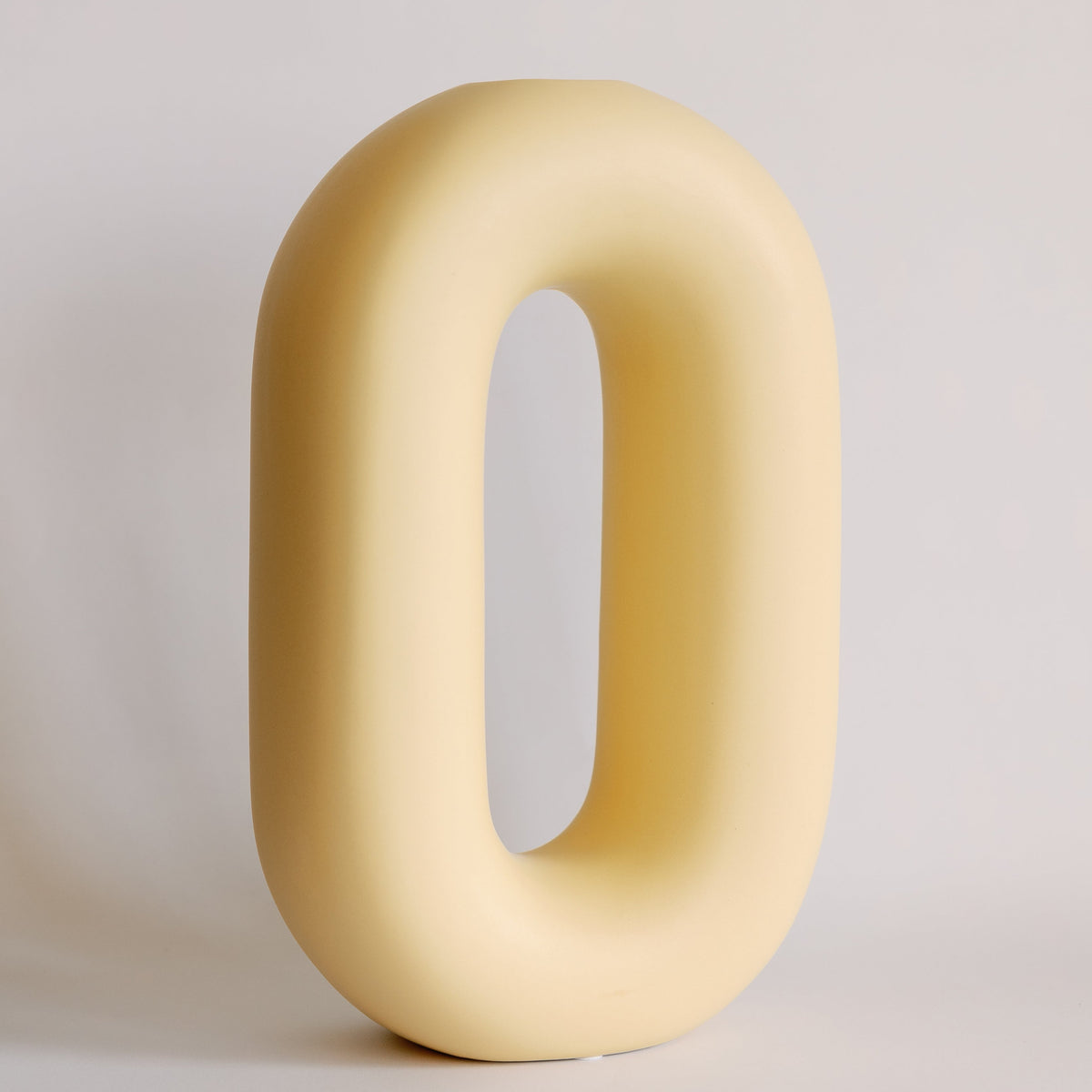 Pale yellow oval loop ceramic bud vase, tall rounded racetrack shape with open center, matte glaze front view