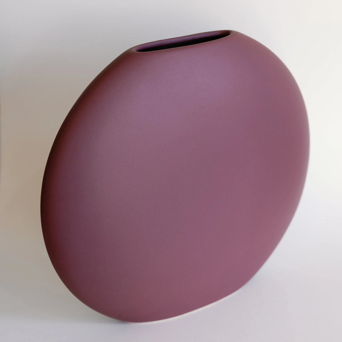 Luna ceramic vase in plum shown at an angle, rounded flat body with slender slot opening