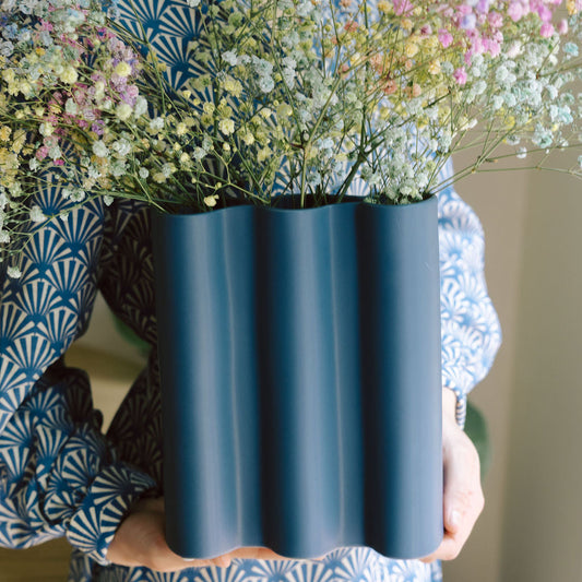 Person holds the blue Cobalt Fluted vase filled with pastel baby's breath, scale shot against patterned dress.