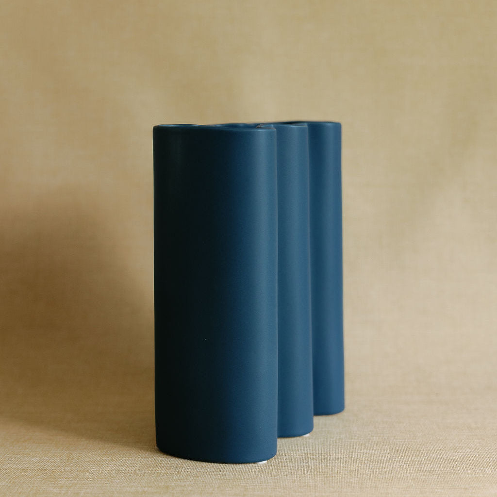 Cobalt Fluted Flower Vase empty, showing its wavy three-lobed silhouette against a tan linen backdrop.