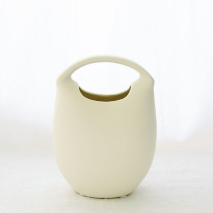 Ivory ceramic basket bud vase with curved top handle, shown empty against a soft white backdrop.