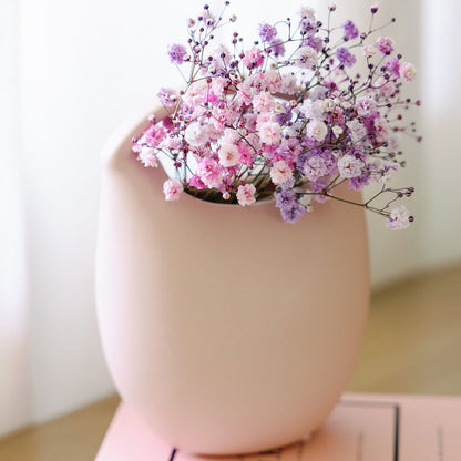 Blush pink ceramic basket bud vase holding pink and purple baby's breath, styled on stacked fashion books.