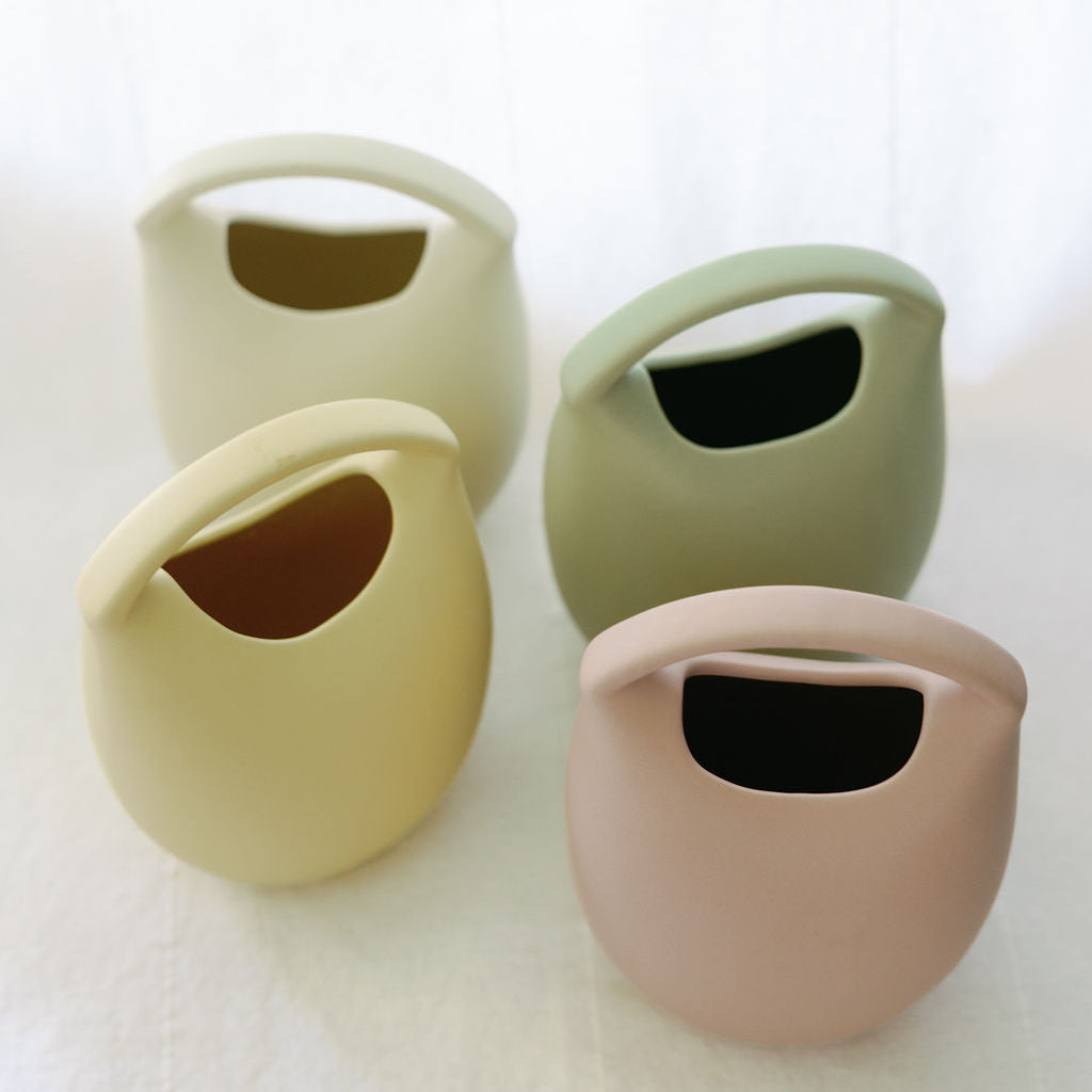 Four ceramic basket bud vases in yellow, sage, green and blush, grouped to show the color range.