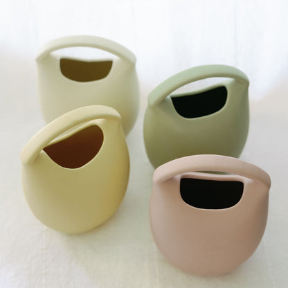 Four ceramic basket bud vases in yellow, sage, green and blush, grouped to show the color range.