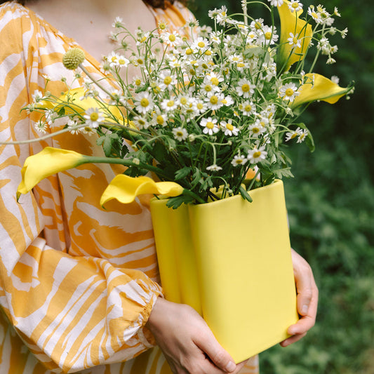 Person holding a yellow container filled with flowers against a blurred green background