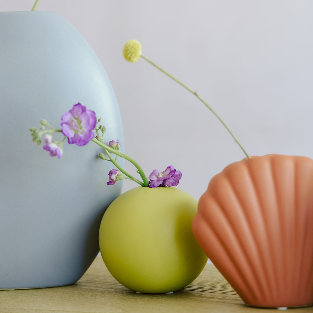 Green round Mini Orb Bud Vase with purple stock flowers, styled beside blue and terracotta shell vases.