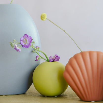Green round Mini Orb Bud Vase with purple stock flowers, styled beside blue and terracotta shell vases.
