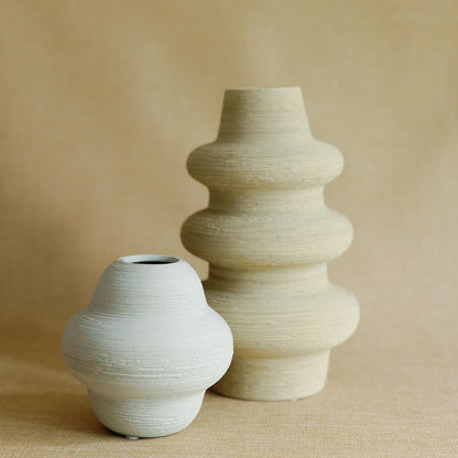 Two ridged Mud Cocoon Ceramic Vases, a small rounded one and a tall tiered form, in cream and beige.