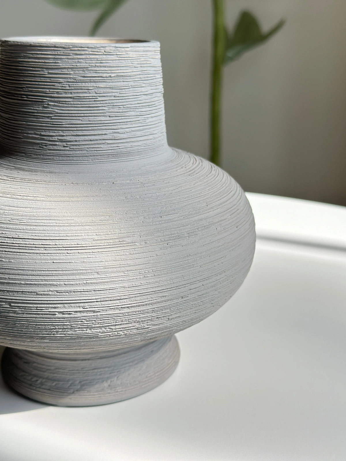 Nesting ceramic vase close-up showing ridged horizontal texture and rounded grey body with footed base