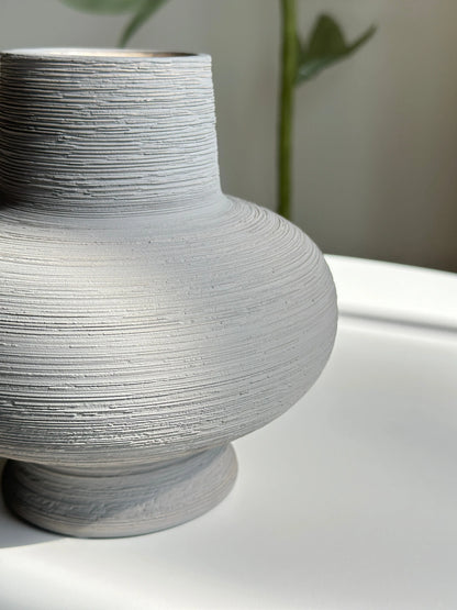 Nesting ceramic vase close-up showing ridged horizontal texture and rounded grey body with footed base