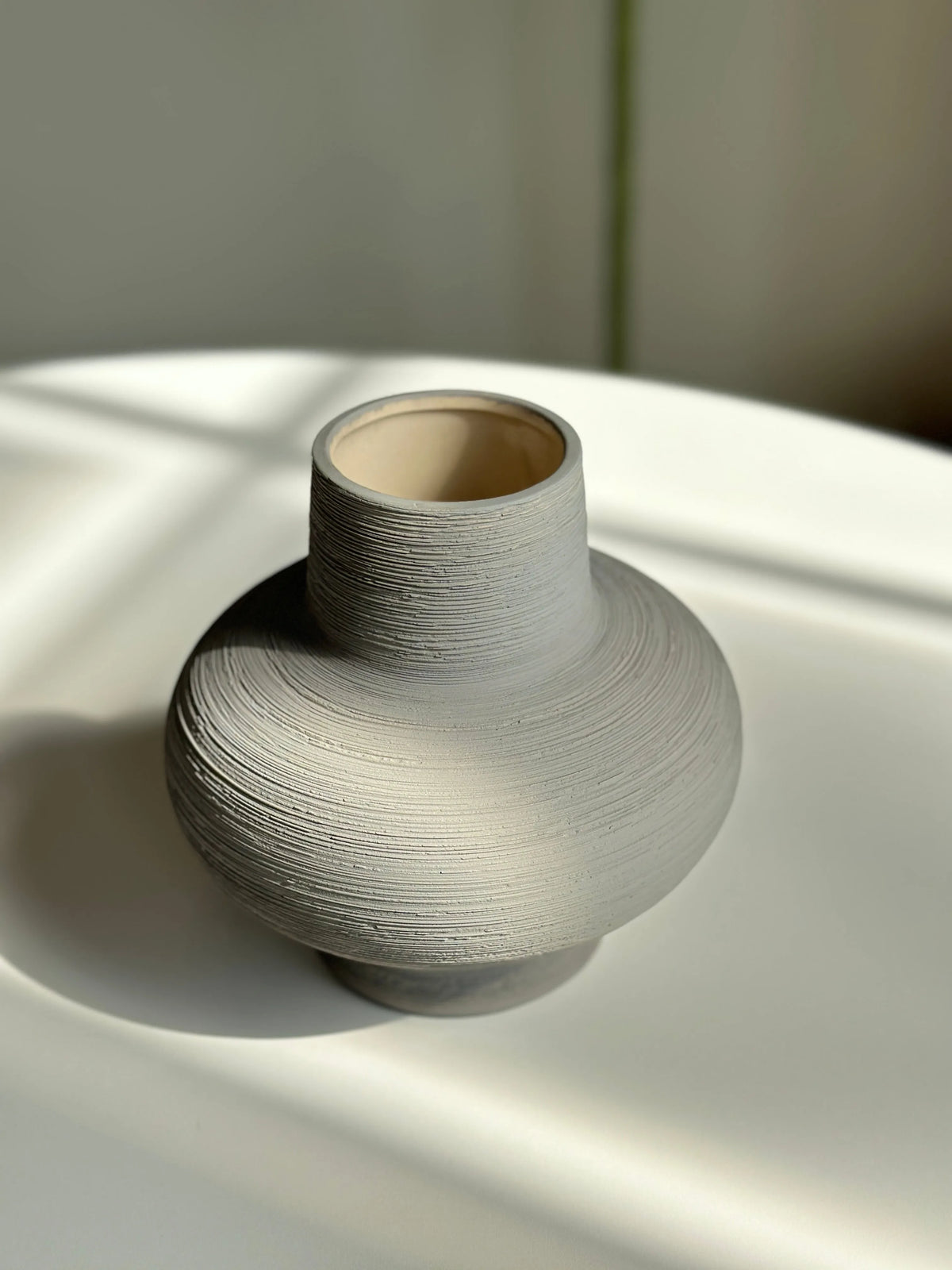 Nesting grey ceramic vase shown full with ribbed body, narrow neck and exposed clay interior in soft sunlight