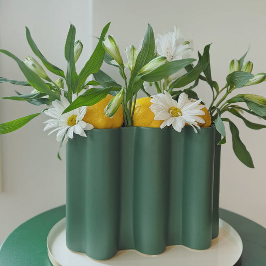Sage green Ripple ceramic vase with wavy edge holding daisies and lemons on a white tray and green table.