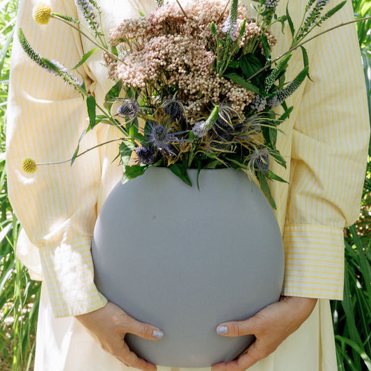Pebble Ceramic Vase in grey held by a woman outdoors, filled with wildflowers and blue thistle, scale shot.