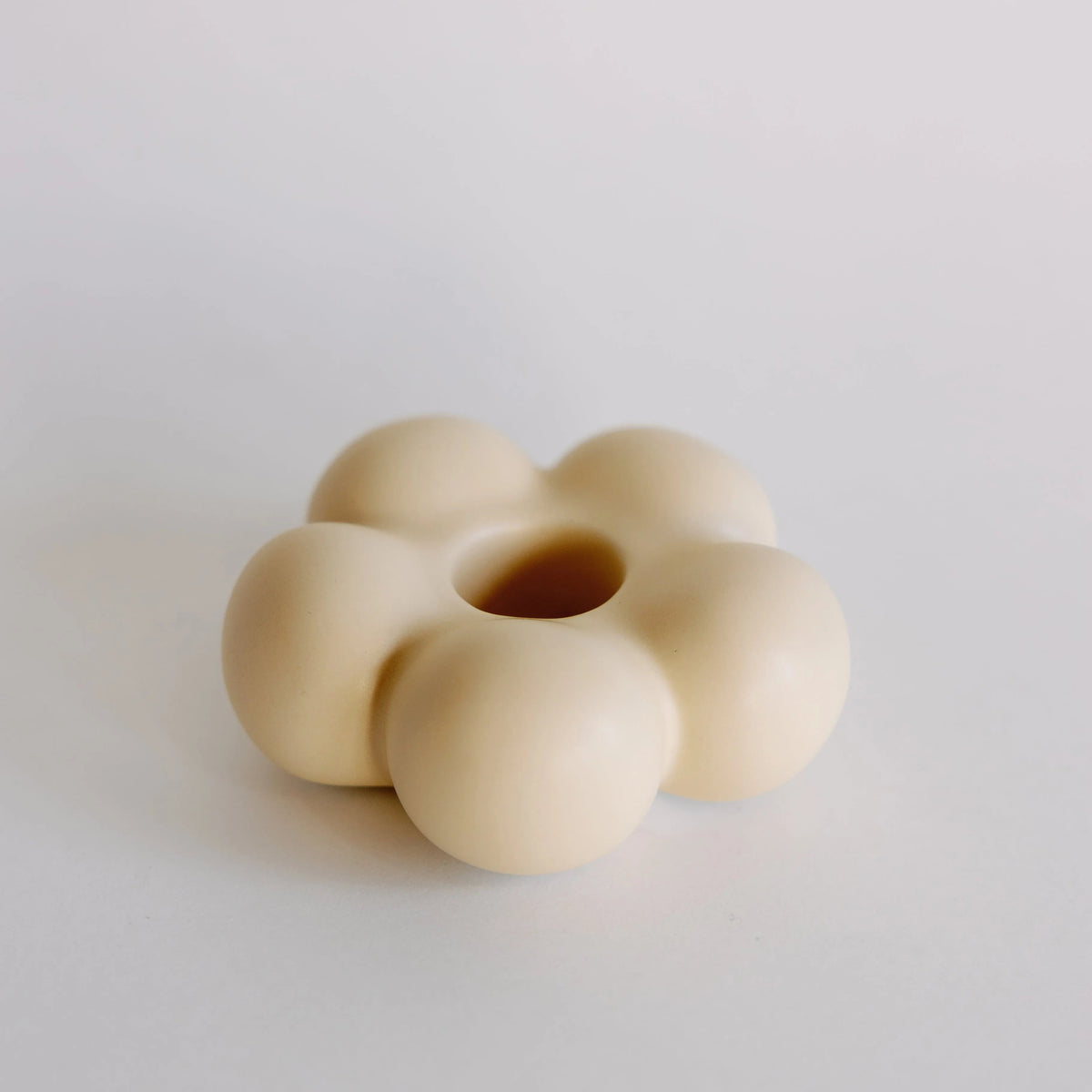 Cream beige flower-shaped ceramic taper candle holder with bubbly petals and center hole, angled full view