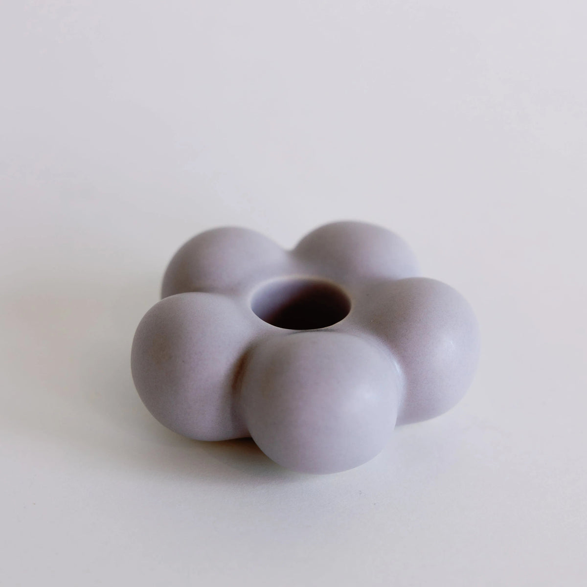 Lilac purple flower-shaped ceramic taper candle holder with rounded petals and center taper hole, full view
