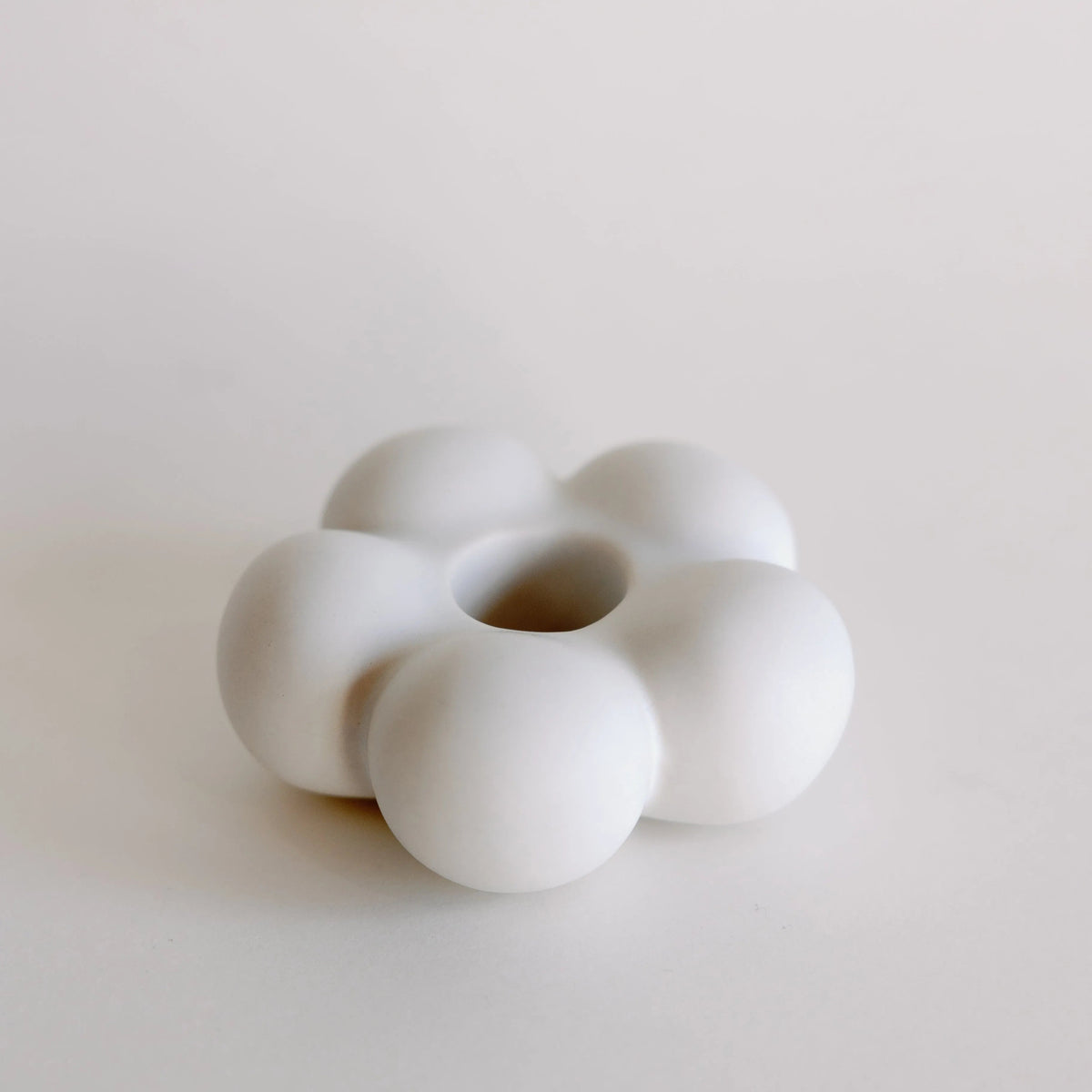 White matte ceramic taper candle holder shaped like a six-petal flower, full product on a pale surface