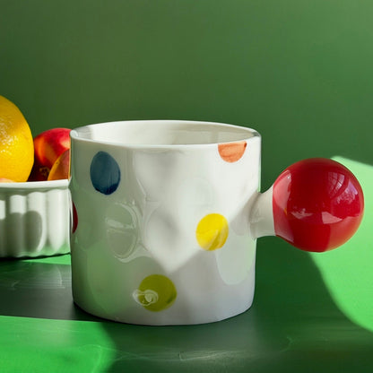 Colorful polka dot mug with a red handle on a green surface
