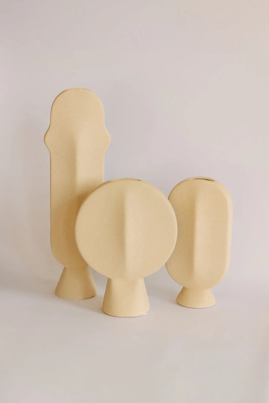 Three sand-beige sculptural ceramic bud vases in tall, round and oval shapes grouped together