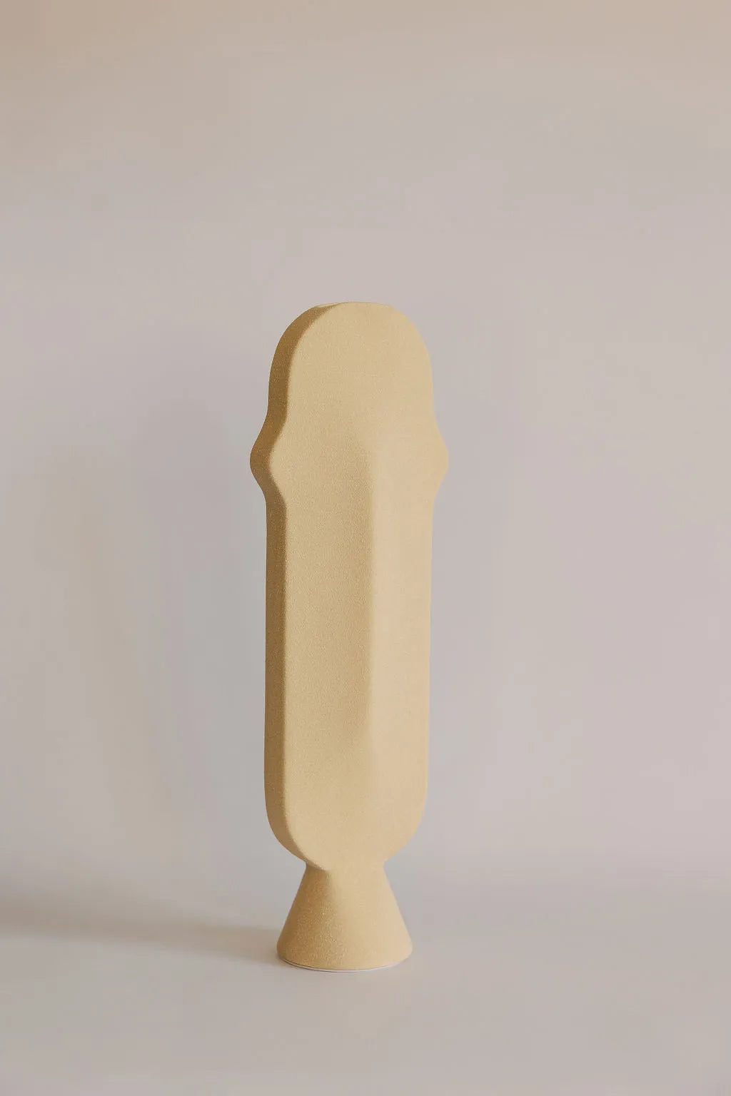 Tall narrow beige ceramic bud vase with arched profile on a small footed base